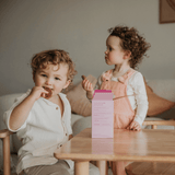 Two children sitting at a table with a pink box in front of them.
