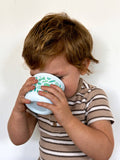 Child holding a white cup with green designs close to their face against a plain background