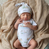 Newborn baby in a floral hat and romper lying on a beige blanket