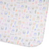 Close-up of a baby mattress protector or fitted sheet with a colorful seashell and starfish pattern on a white background. A small white tag on the upper right corner shows the brand 'mima'.