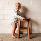 Child standing on a small wooden stool against a white tiled wall.