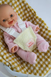 Baby doll in a pink outfit with a yellow baby carrier on a checkered blanket
