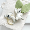 Two white koala-shaped baby teether toys on a white surface with green leaves.