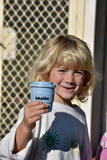 Child holding a blue cup with 'bbeeine' branding in front of a lattice background
