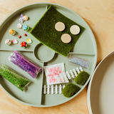 Green tray with various miniature garden accessories on a wooden surface