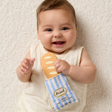 Baby holding a toy bread and bag on a soft surface