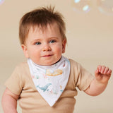 A baby wearing a beige short-sleeve shirt and a white triangular bib with a colorful underwater print, photographed against a warm beige background with soft bubble-like lights.