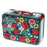 A Ladybird Metal Case featuring a dark teal blue background decorated with a colorful pattern of red ladybugs, yellow and pink flowers, and green leaves. It has a red handle, silver metal latches, and a round blue hanging tag.