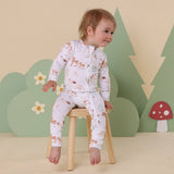 Child wearing a patterned outfit sitting on a stool with a forest-themed background