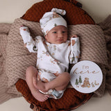 Newborn baby in a floral outfit with a 'I'm here' sign on a brown textured surface