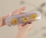 Hand holding a clear case with yellow flowers and 'BARE MUM' text against a blurred background