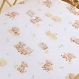 A close-up of a white fabric cover with a repeating watercolor-style print of baby sheep, chicks, bails, and small green leaves, laid over a woven chair.