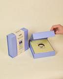 Product packaging with a gold disc and purple box on a beige background