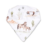 A white triangular bandana bib with a western-themed print featuring horses, cacti, and desert trees, finished with two metal eyelets at the top.