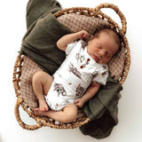 Newborn baby sleeping in a woven basket with a green blanket and animal-patterned outfit.
