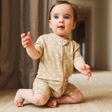 Baby in a beige onesie with white polka dots sitting on a wooden floor.