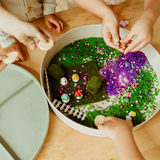 Children playing with a decorative garden scene on a wooden table