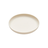 A minimalist, shallow round plate in a warm cream or off-white color, shown from a top-down perspective on a solid white background.