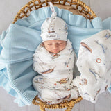 Newborn baby swaddled in a nautical-themed blanket with a matching hat, lying on a textured blanket.