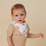 A baby wearing a beige short-sleeve romper and a white bandana bib with a brown rocking horse and red bow print, posed against a solid beige background.