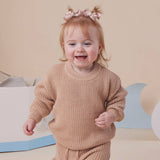 Child wearing a beige knit outfit with a happy expression on a neutral background