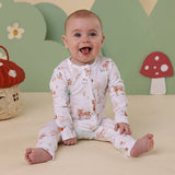 Baby wearing a forest-themed onesie sitting on a beige surface with a green wall and mushroom decorations in the background.