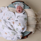 Newborn baby wrapped in a patterned blanket with a 'I'm here' sign, lying on a textured surface.