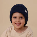 Child wearing a navy blue knit hat with a visible brand logo on a beige background