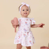 Baby girl in a floral dress holding pink items against a beige background