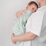 Person holding a baby wrapped in a light green blanket with white patterns against a plain background