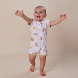 A baby wearing a white short-sleeve footless romper with a cute teddy bear print, standing on a beige background with arms outstretched.