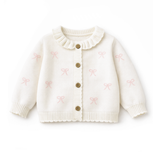 White cardigan with pink bow patterns and gold buttons on a white background