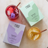 Two boxes of 'mini + me' Hydramama with a red drink and a yellow dessert on a light surface.