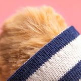 Close-up of a dog wearing a blue and white striped sweater against a pink background