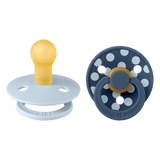 Two baby pacifiers, one yellow and light blue, the other navy with white polka dots, on a white background.