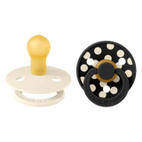 Two baby pacifiers, one beige and white, the other black with white polka dots, on a white background.