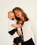Woman holding a baby with a pacifier against a plain background