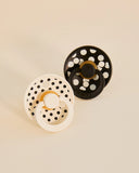 Two black and white polka dot baby teething rings on a beige background