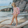 Person in a pink swimsuit with orange patterns standing on a log at the beach.