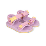 A pair of children's pink sandals with yellow accents, featuring adjustable straps and a yellow brand plaque on the footbed, set against a plain white background.
