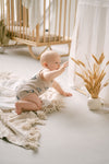 Baby in a crib with a decorative plant and white curtains in a bright room