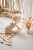 Baby in a crib with a decorative plant and white curtains in a bright room