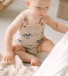 Baby wearing a beige romper with zebra patterns sitting on a soft surface.