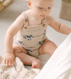 Baby wearing a beige romper with zebra patterns sitting on a soft surface.