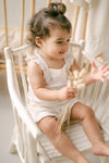 Child sitting on a white chair holding dried flowers in a softly lit room.
