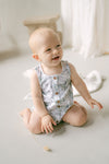 Baby sitting on a light-colored floor wearing a floral romper.