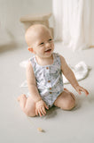 Baby sitting on a light-colored floor wearing a floral romper.