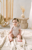 Baby sitting on a textured blanket in a softly lit room with neutral decor.