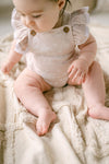 Baby in a beige romper sitting on a soft surface