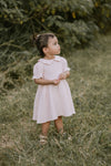 Young girl in a pink dress standing in a grassy field with trees in the background